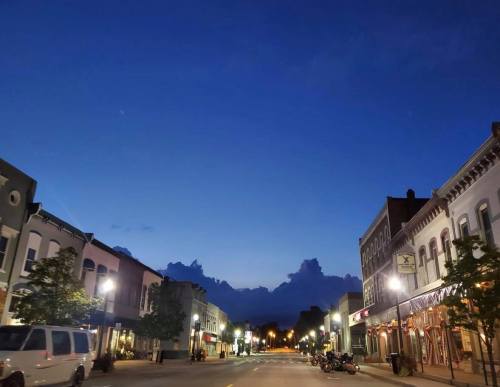 A quiet downtown street at dusk, with buildings lining the road and a deep blue sky filled with clouds.