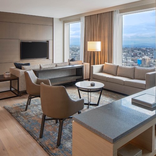 Modern hotel suite featuring a cozy seating area, large windows with city views, and stylish decor.