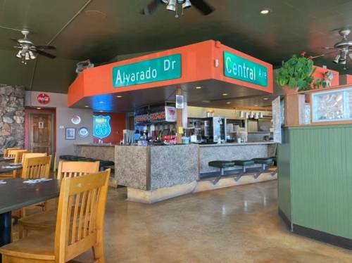 Interior of a restaurant featuring a counter with signage for Alvarado Dr and Central Ave, wooden tables, and a casual atmosphere.