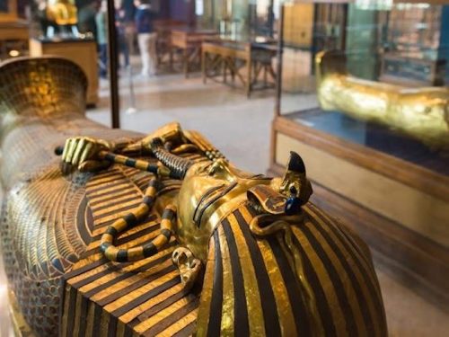 A close-up of a golden sarcophagus with intricate designs, displayed in a museum setting.
