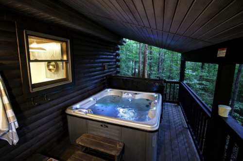 A cozy hot tub on a wooden deck surrounded by trees, with a window showing a glimpse of the interior.