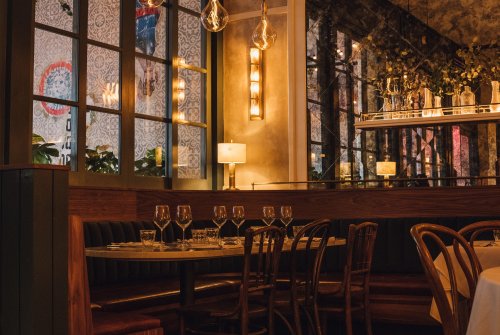 Cozy restaurant interior with wooden seating, elegant lighting, and a mirrored wall, set for dining with glassware.