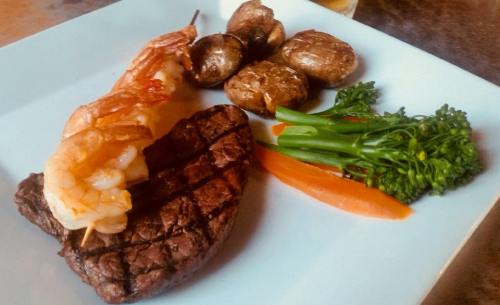 A plate featuring grilled steak, shrimp skewers, roasted potatoes, and sautéed vegetables.