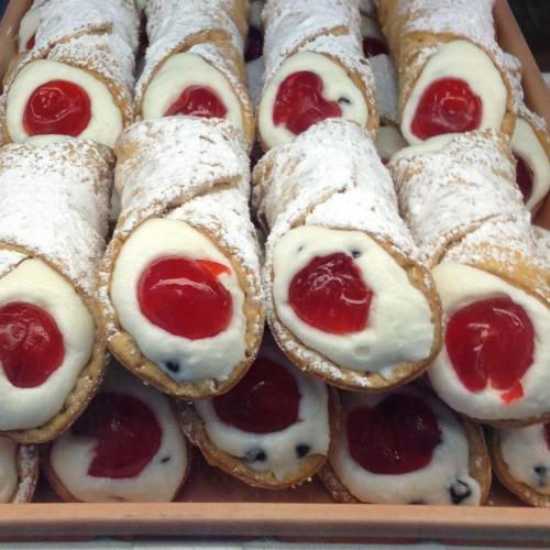 A close-up of cannoli filled with creamy ricotta and topped with a cherry, dusted with powdered sugar.