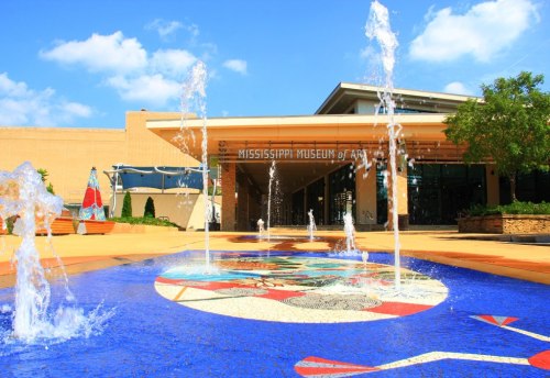 Exterior view of the Mississippi Museum of Art, featuring a colorful fountain and blue sky.