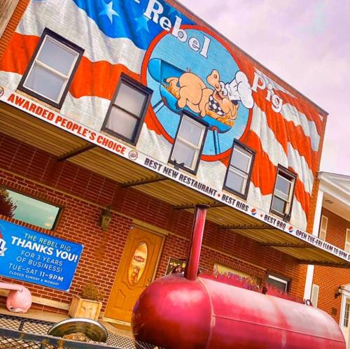 Mural of a pig with chef hat on a building, featuring red, white, and blue stripes; sign for "Rebel Pig" restaurant.