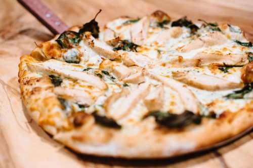A close-up of a pizza topped with sliced chicken, spinach, and melted cheese on a wooden surface.