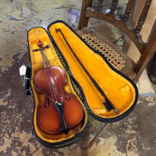 A violin and bow resting in a yellow-lined case, placed on a wooden chair in a rustic setting.