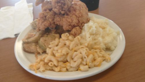 A plate of fried chicken, macaroni and cheese, mashed potatoes, and fried okra on a wooden table.
