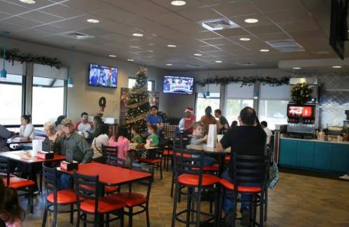 A busy restaurant decorated for Christmas, with families dining and a tree in the corner, and TVs showing sports.