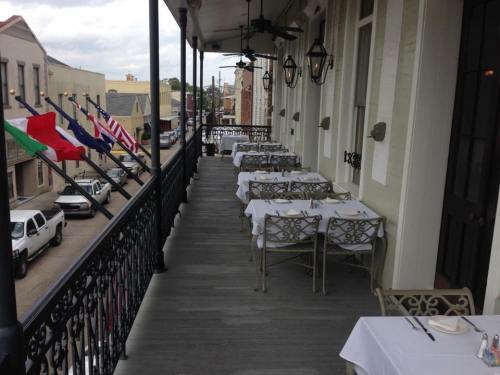 A restaurant balcony with empty tables and chairs, featuring flags and a view of a street lined with parked cars.