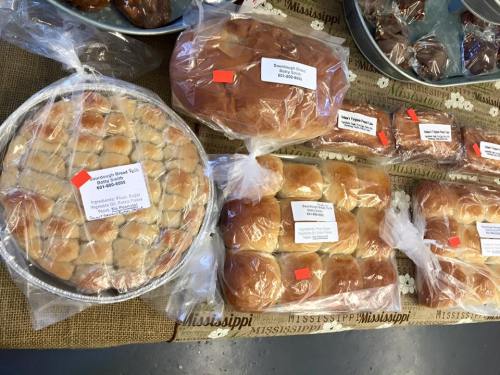 Assorted baked goods wrapped in plastic, including rolls and a pie, displayed on a burlap tablecloth.