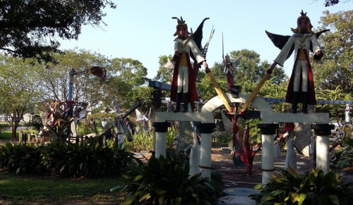A vibrant outdoor sculpture garden featuring large, colorful statues and lush greenery under a clear blue sky.