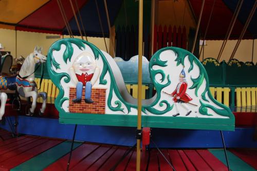 Colorful carousel featuring whimsical characters, including a seated figure and a soldier, with vibrant decorations.