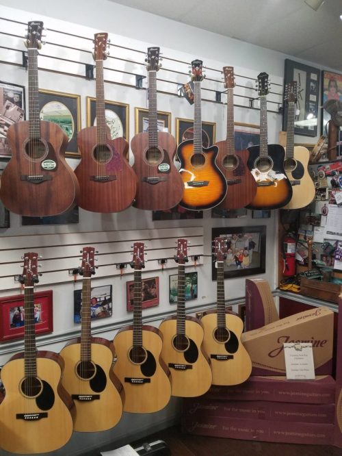 A display of various acoustic guitars hanging on a wall, with framed photos and memorabilia in the background.