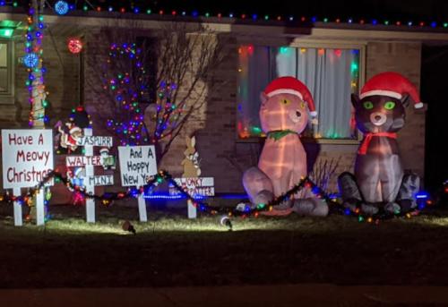 A festive yard display with inflatable cats and signs wishing a "Meowy Christmas" and "Happy New Year."