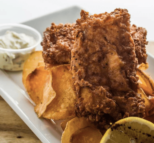 Crispy fried chicken served with golden potato chips and a side of dipping sauce and a lemon wedge.
