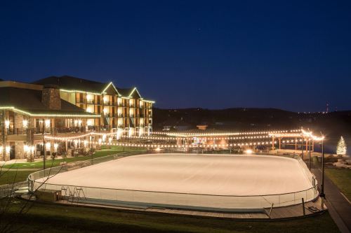 A lit outdoor ice skating rink at night, surrounded by a hotel and festive string lights.