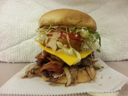 A towering burger with lettuce, tomato, cheese, bacon, and grilled onions on a soft bun, served on a paper napkin.