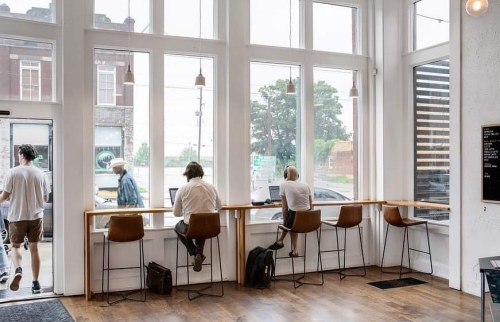 A modern café interior with large windows, featuring people working at a counter and others walking outside.
