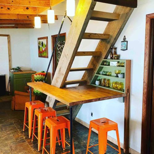 A cozy interior featuring a wooden staircase, a table with orange stools, and decorative shelves.