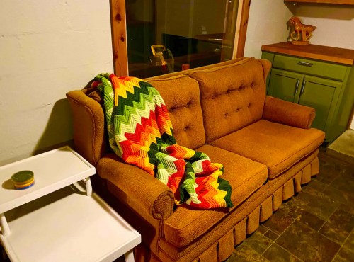 A cozy living room scene featuring a brown couch draped with a colorful zigzag blanket and a small white side table.