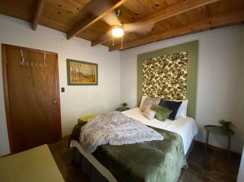 Cozy bedroom with a green accent wall, floral headboard, and wooden ceiling beams, featuring a bed and small side table.