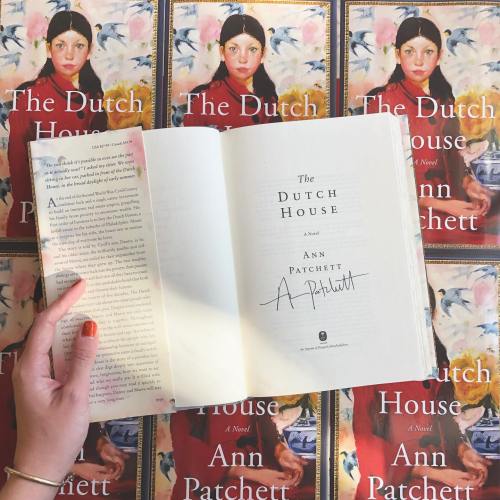 A hand holds an open book titled "The Dutch House" by Ann Patchett, surrounded by multiple copies of the book's cover.