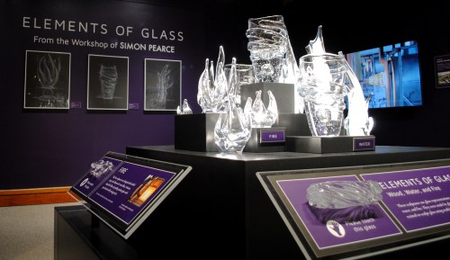Display of glass sculptures titled "Elements of Glass" by Simon Pearce, featuring pieces representing fire and water.