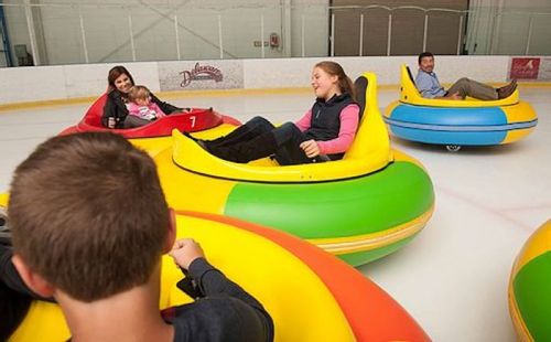 A group of people enjoying bumper cars on ice, smiling and having fun in colorful inflatable vehicles.