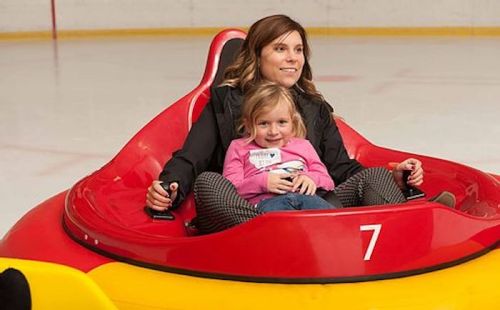 A woman and a young girl smile while riding in a colorful bumper car on an ice rink.