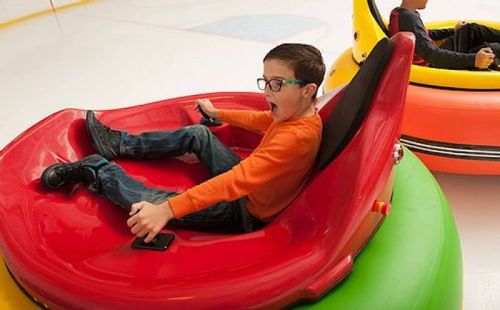 A boy in an orange shirt enjoys riding a red bumper car on an ice rink, with another bumper car in the background.
