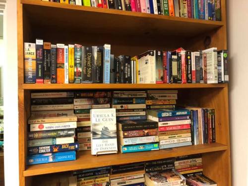 A wooden bookshelf filled with various books, including titles by Ursula K. Le Guin and other authors.