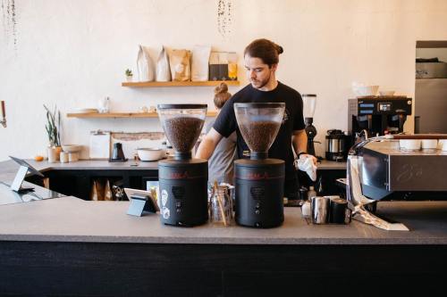 A barista prepares coffee at a modern café with coffee grinders and a sleek counter in the background.