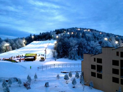 A snowy ski slope illuminated by lights, with a hill in the background and a building in the foreground.