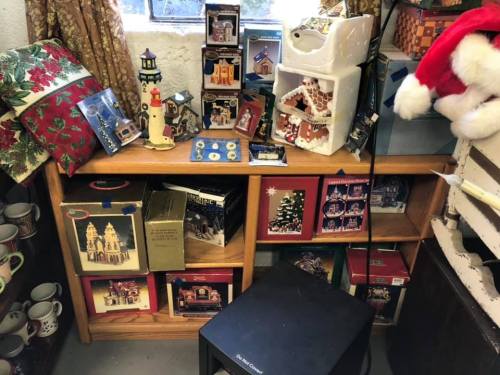 A cluttered shelf filled with holiday decorations, including miniature houses, ornaments, and festive wrapping.