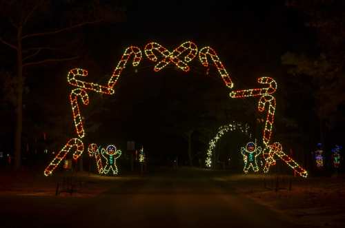 Colorful candy cane archway with festive lights, welcoming visitors to a holiday display at night.