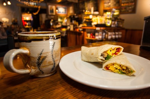 A plate with two breakfast burritos and a coffee mug, set in a cozy café with a warm atmosphere.