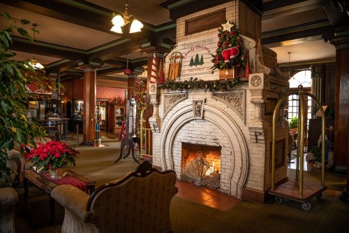 Cozy lobby with a decorated fireplace, festive plants, and vintage furnishings, creating a warm holiday atmosphere.