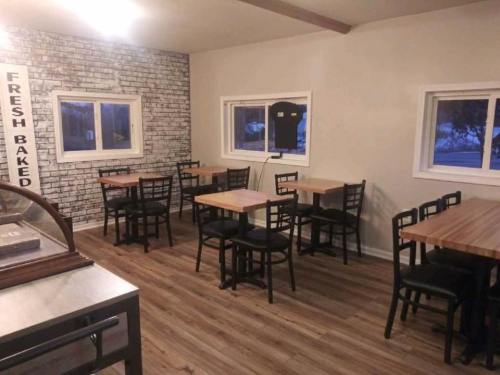 A cozy restaurant interior with wooden tables, black chairs, and a brick accent wall. Windows let in natural light.
