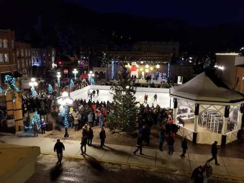 A bustling outdoor ice skating rink at night, surrounded by festive lights and a crowd enjoying the holiday atmosphere.