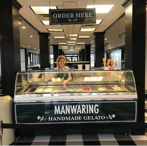 A gelato shop with a display case filled with colorful gelato flavors and a staff member ready to serve.