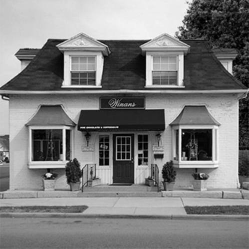 A charming, historic building with a black awning reading "Whinans," featuring large windows and a welcoming entrance.