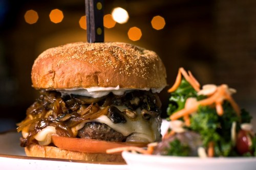 A juicy burger with melted cheese, sautéed onions, and a side salad on a plate, set in a warm, inviting atmosphere.