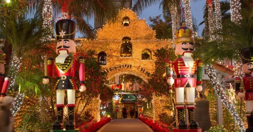 A festive entrance adorned with colorful lights and large nutcracker decorations, surrounded by palm trees.