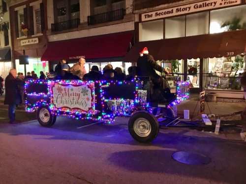 A festive parade float decorated with colorful lights and a "Merry Christmas" sign, with people enjoying the ride.