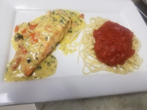 A plate featuring salmon in a creamy sauce with diced tomatoes, served alongside spaghetti topped with marinara sauce.