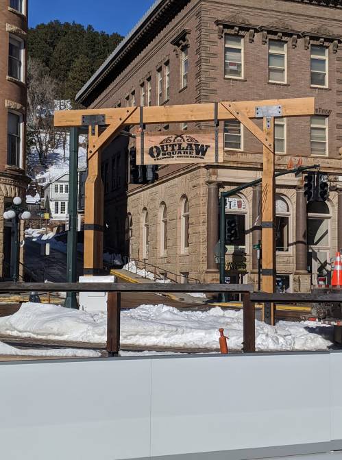 Wooden archway with "Outlaw" sign, snowy street scene, historic buildings in the background.