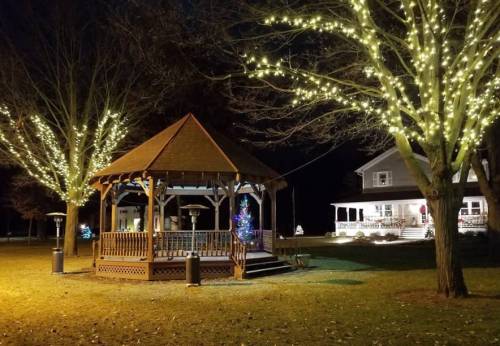 A gazebo adorned with lights, surrounded by trees with glowing decorations, set in a park at night.