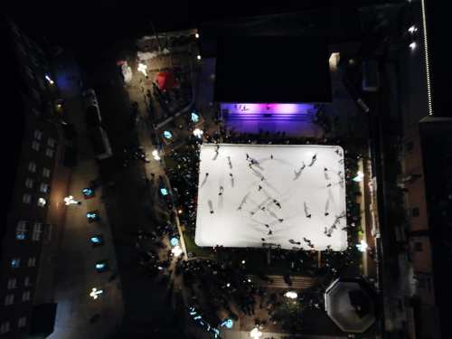 Aerial view of an ice skating rink surrounded by people, with colorful lights and festive decorations.